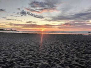 En strand vid solnedgången, med solen som går ner bakom horisonten.