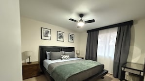 Ein Schlafzimmer mit einem Bett, Nachttischen, einem Deckenventilator und gerahmten Kunstwerken an der Wand.