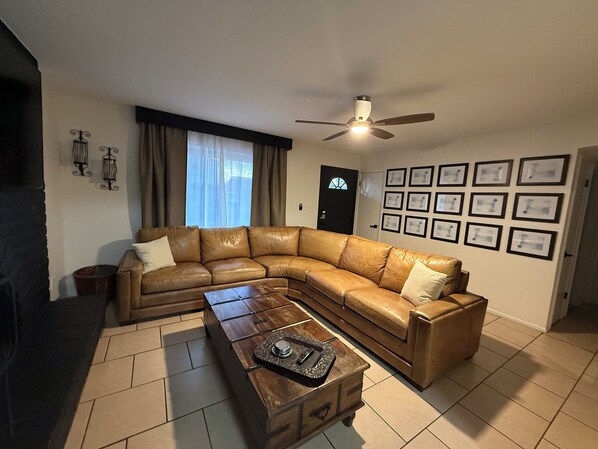 A living room with a L-shaped leather sofa, a wooden coffee table, a ceiling fan, and a door with a window. - Concert lovers and west Gate entertainment. (Phoenix)
