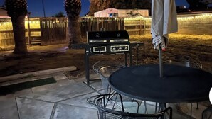 Eine Terrasse im Freien mit Grill, Stühlen und Sonnenschirm.
