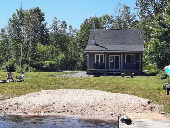 A house with a deck, a small dock, and a sandy area near a body of water. - Private Winter Lakefront Cottage - Relax & Unwind (Port Loring)