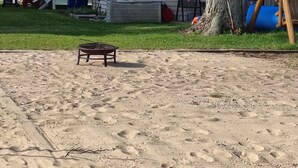 Ein sandiger Bereich mit einem Metalltisch, einem Baum und einem Haus im Hintergrund.