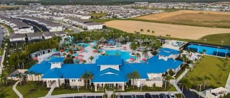 An aerial view of a resort with multiple buildings, a central pool area, and a large parking lot.