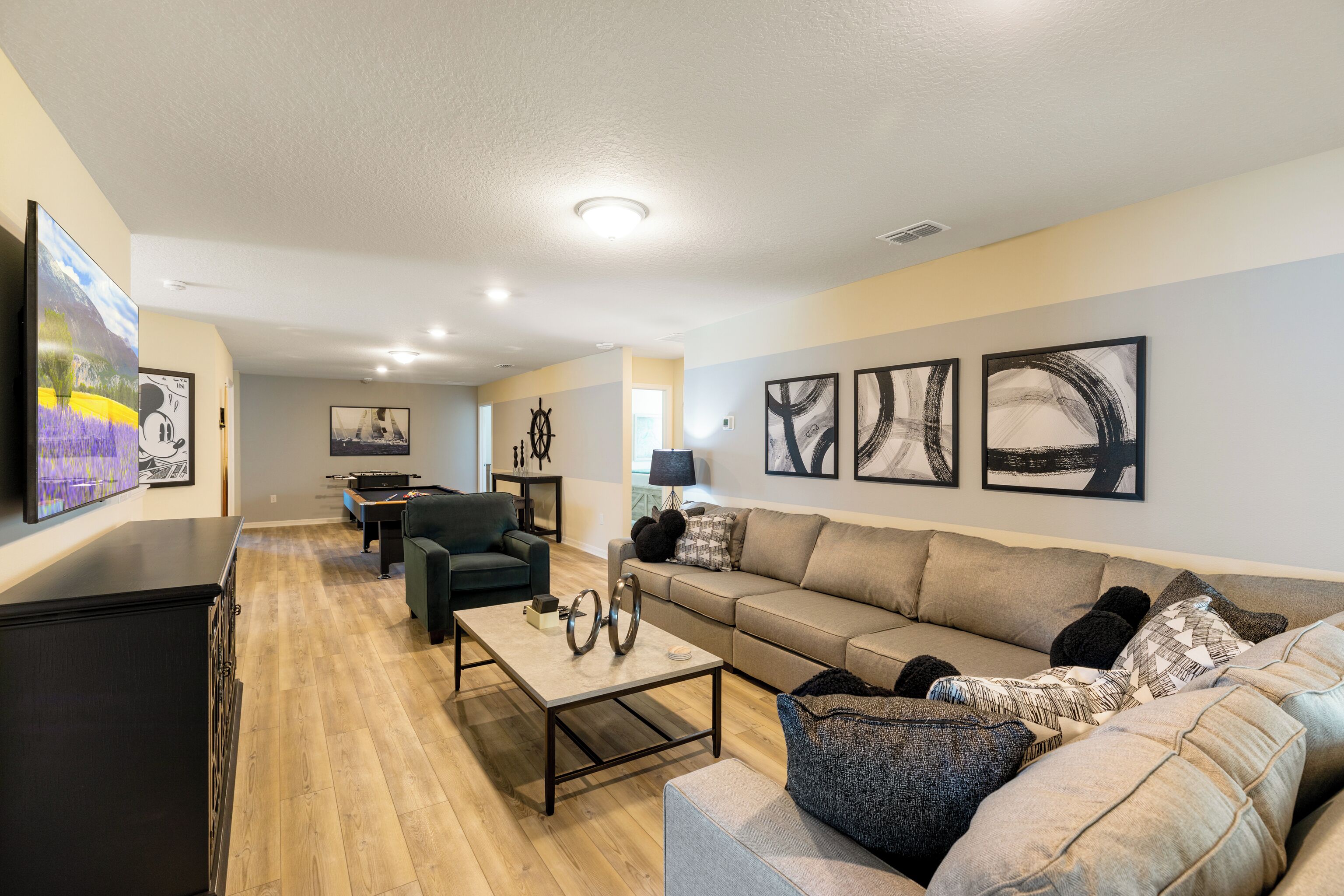 A living room with a sofa, coffee table, and TV. There are framed pictures on the wall and a lamp on a side table.