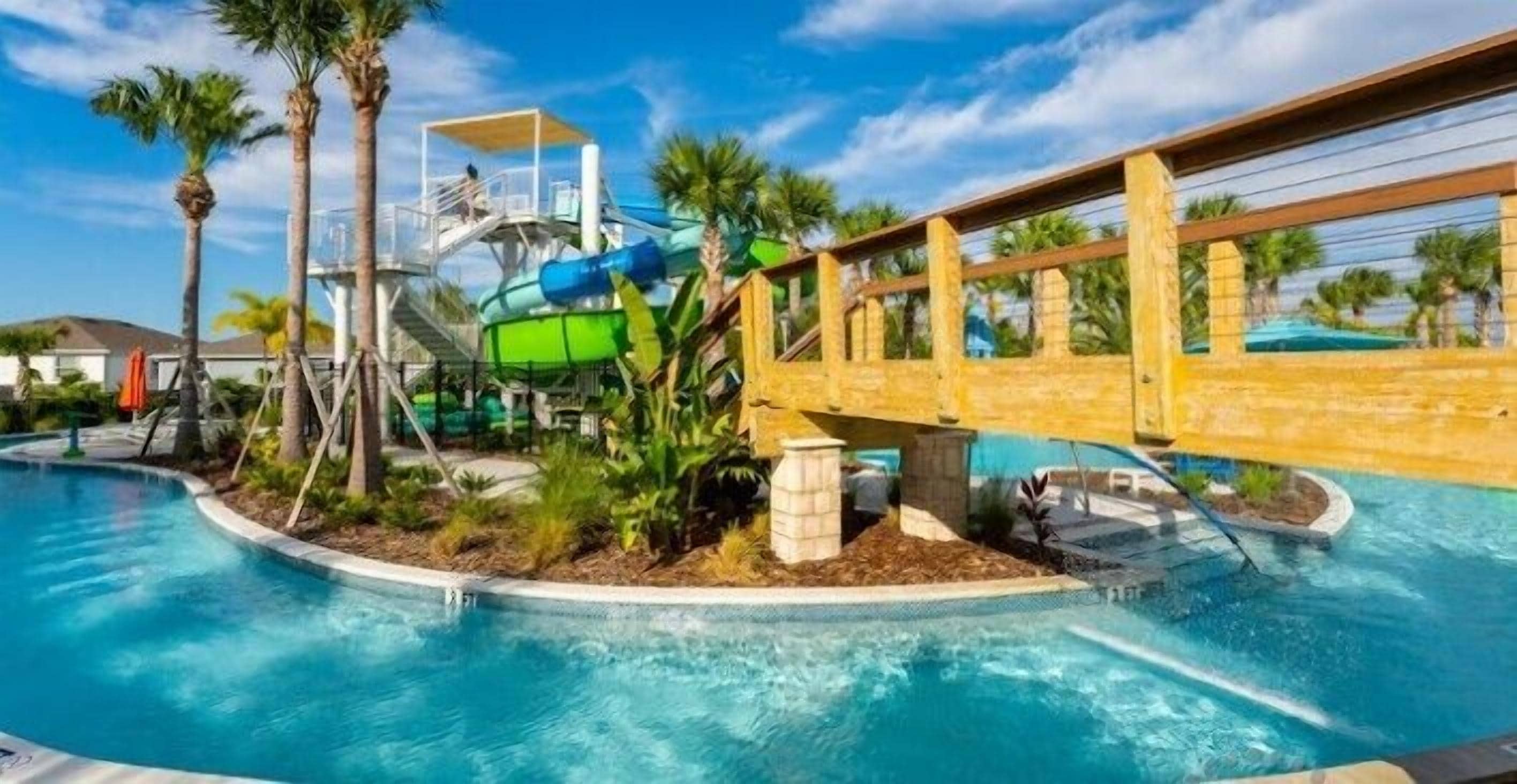 Una piscina con tobogán de agua, palmeras y un puente de madera.