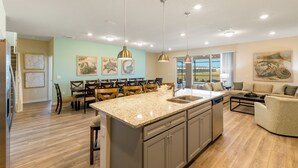 A spacious kitchen with a central island, dining area with chairs, and a living room with a sofa and coffee table.
