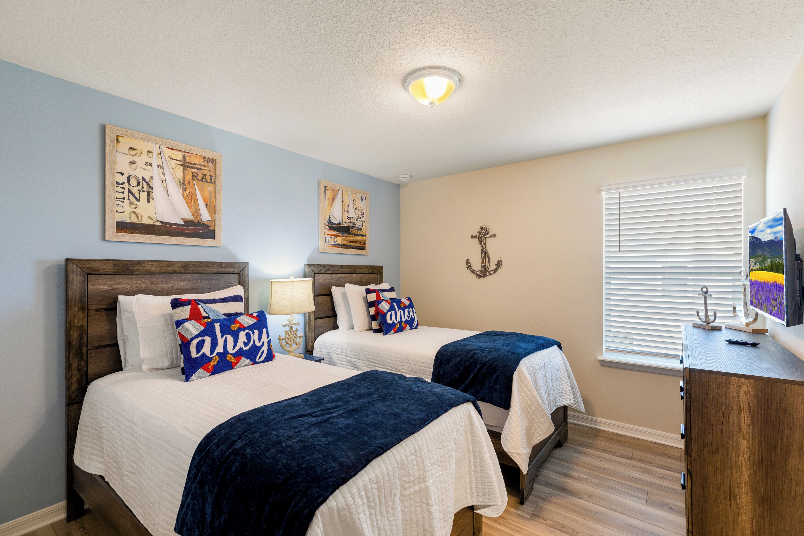 A bedroom with two beds, a wooden headboard, a nightstand, a lamp, a TV, and a window with blinds.