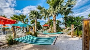 A beach area with hammocks, palm trees, and umbrellas.
