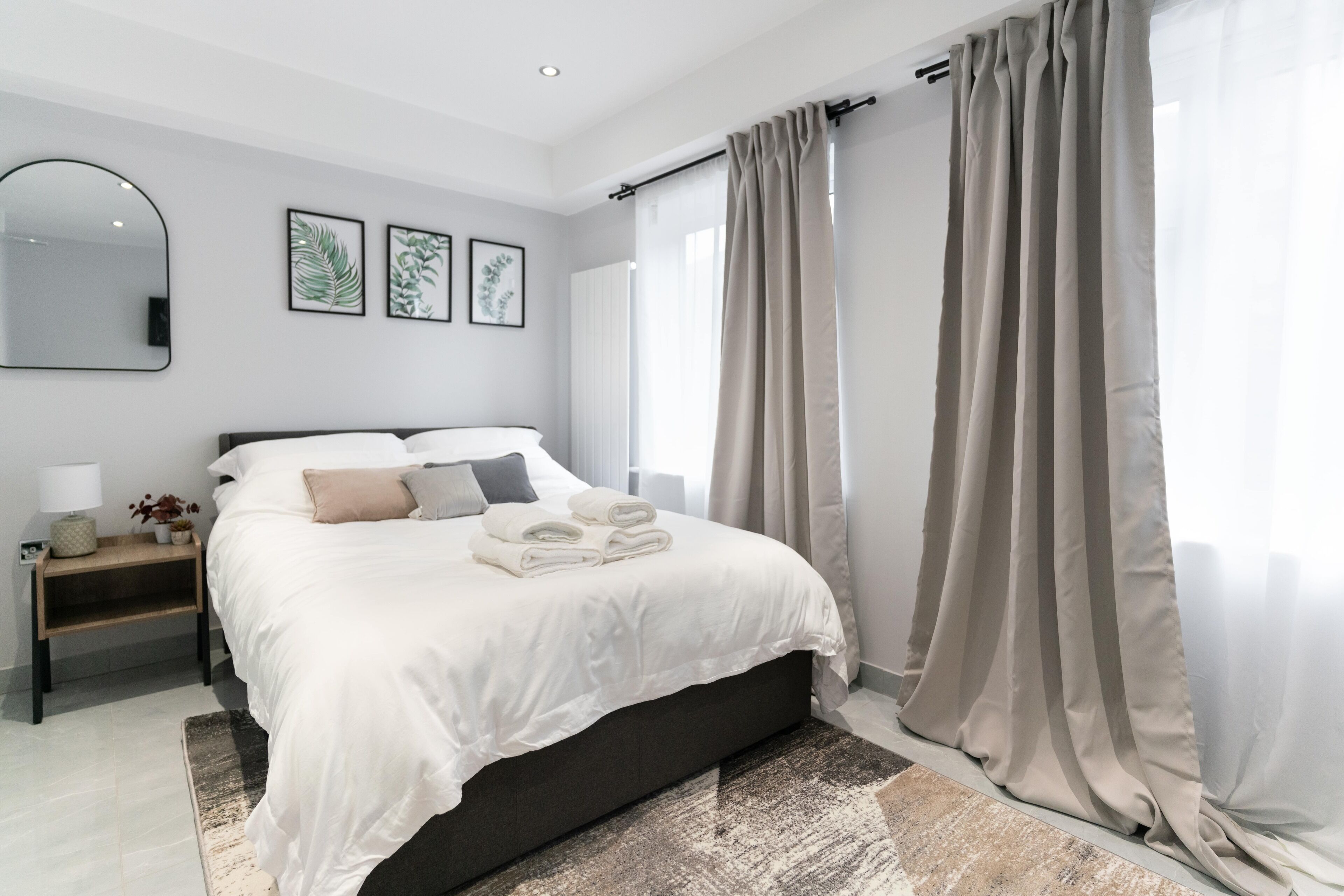 A modern bedroom with a bed, bedside tables, a mirror, and curtains.