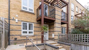 En flervåningsbostadsbyggnad med en fasad av tegel, balkonger och en liten trädgårdsyta med en palmpalm.