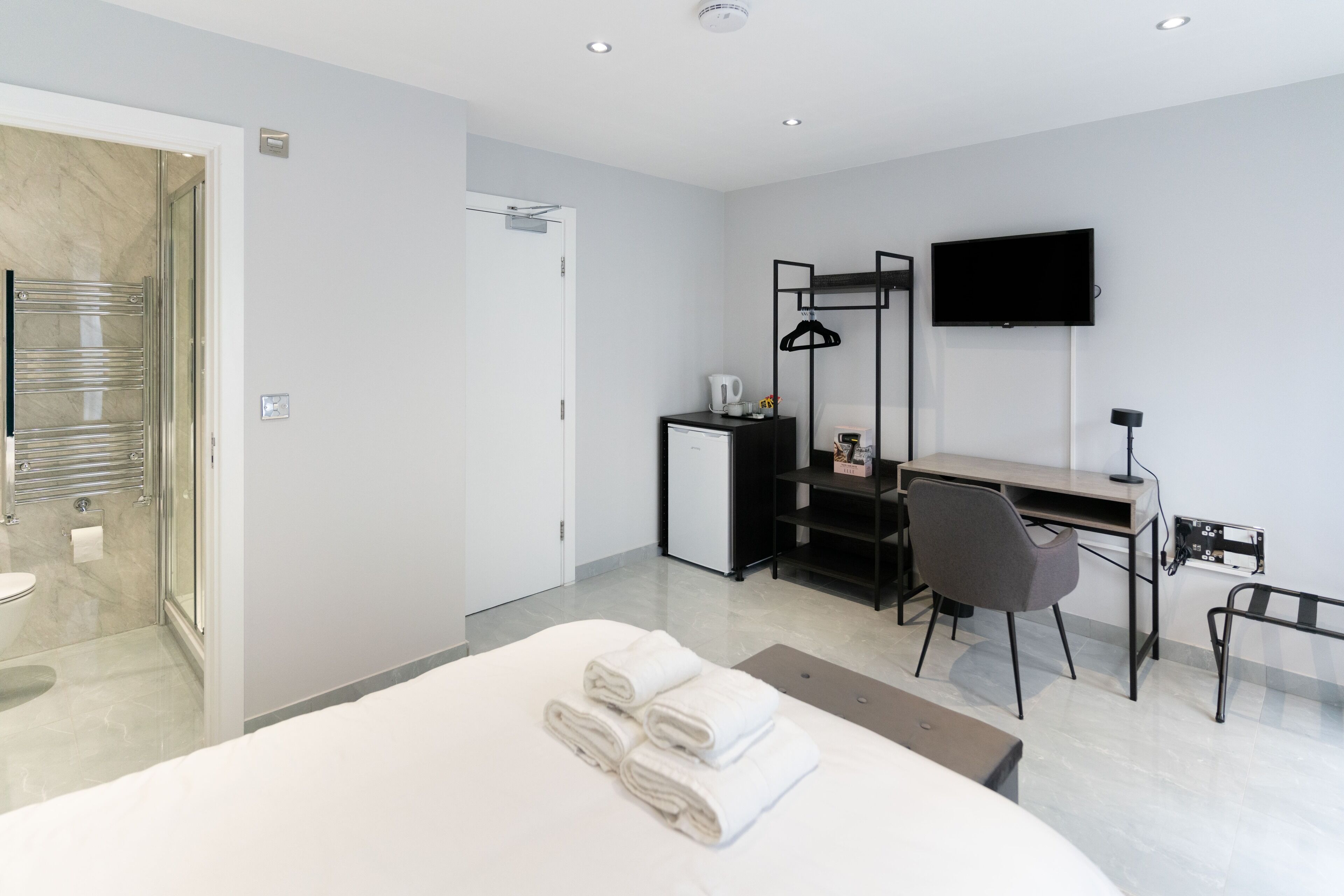 A modern hotel room with a bed, a desk, a chair, a TV, and a shower area.