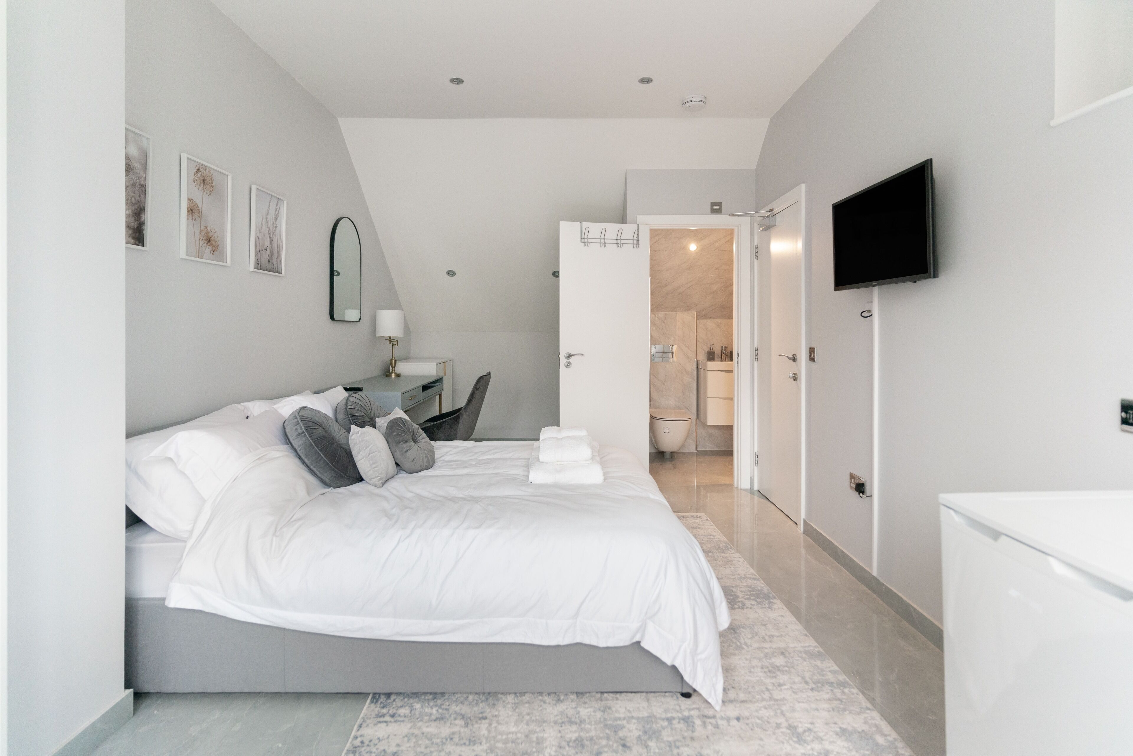 A modern bedroom with a large bed, bedside tables, a TV, and a bathroom visible through an open door.
