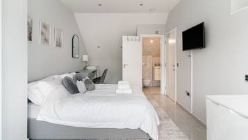 A modern bedroom with a large bed, bedside tables, a TV, and a bathroom visible through an open door.