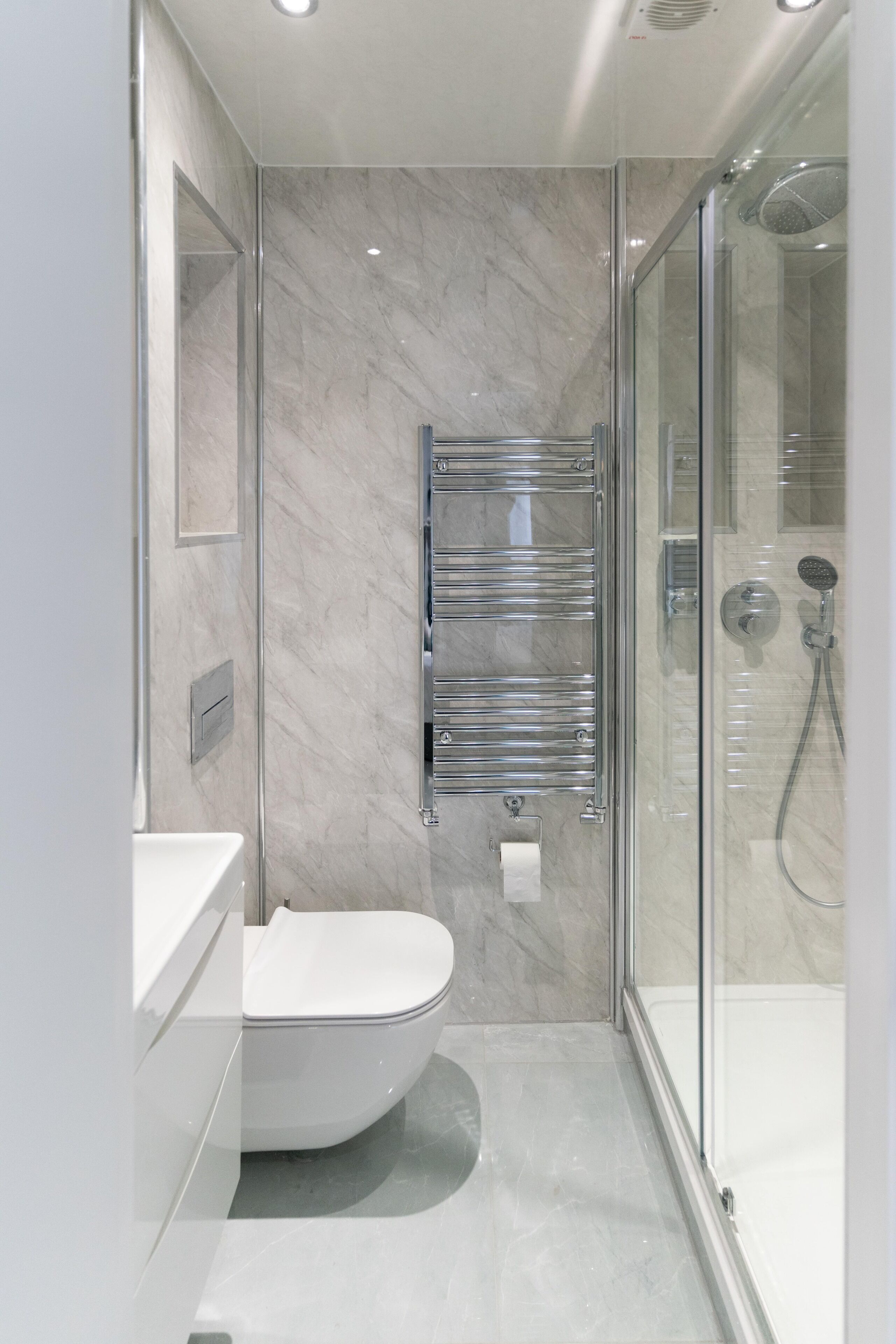 Un baño moderno con ducha de vidrio, inodoro blanco y pared de mármol.