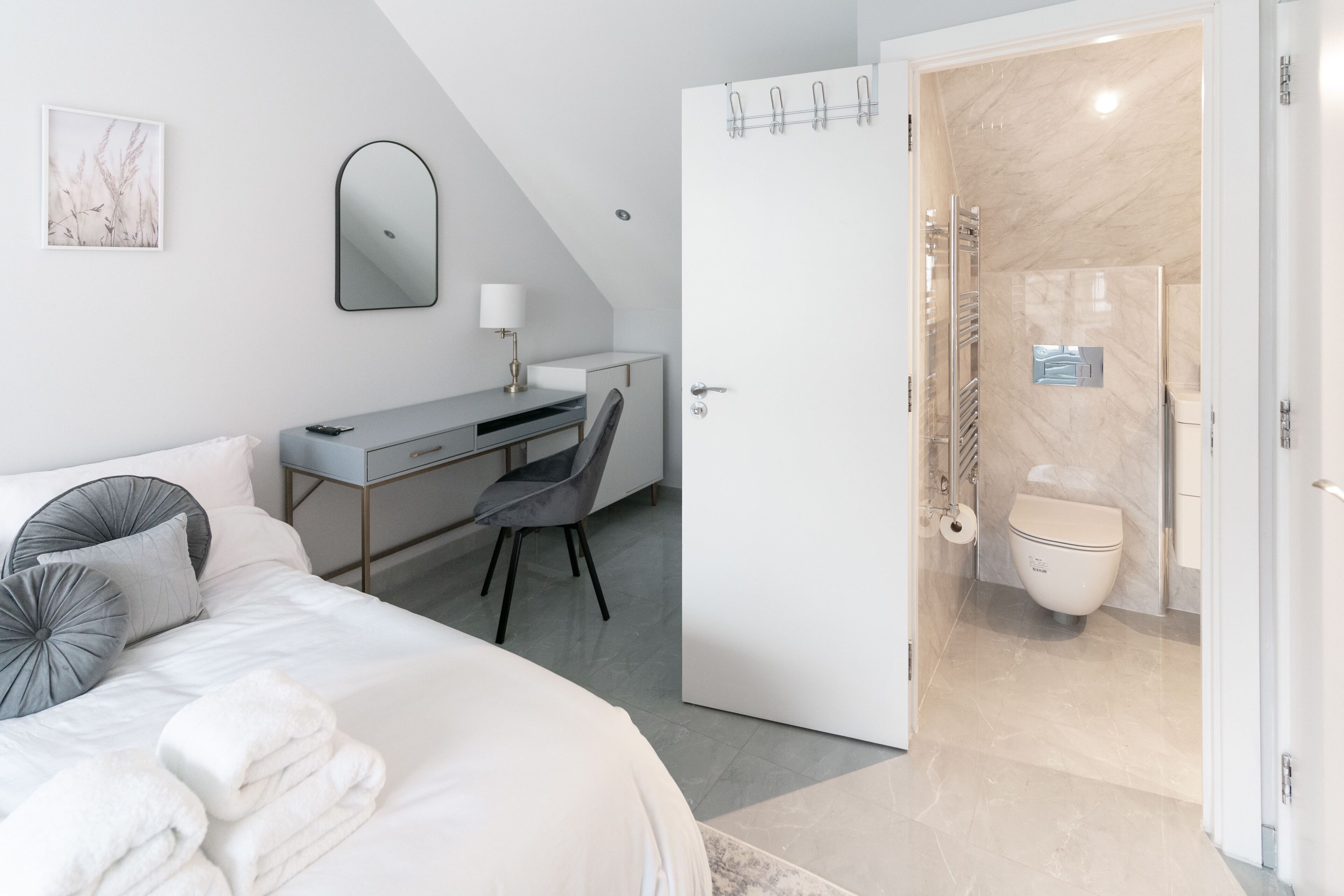 A modern hotel room with a bed, desk, chair, and a bathroom with a shower and toilet.