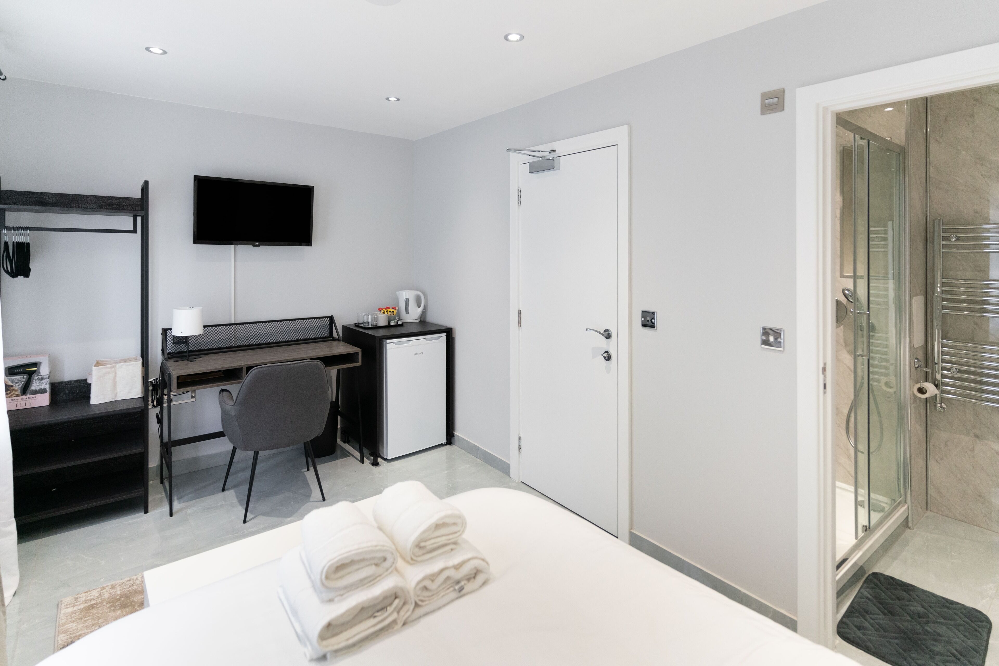 A modern hotel room with a bed, a desk with a computer, a TV, and a shower area.