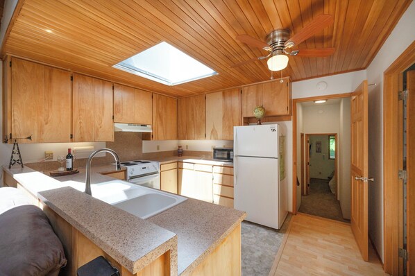 A compact kitchen with wooden cabinets, a central island, a microwave, and a refrigerator.