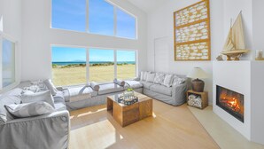 A spacious living room with a large window overlooking a beach, a fireplace, and a sailboat decoration. - Beachfront Villa w/ Direct Beach Access & Elevator!  (Oxnard)