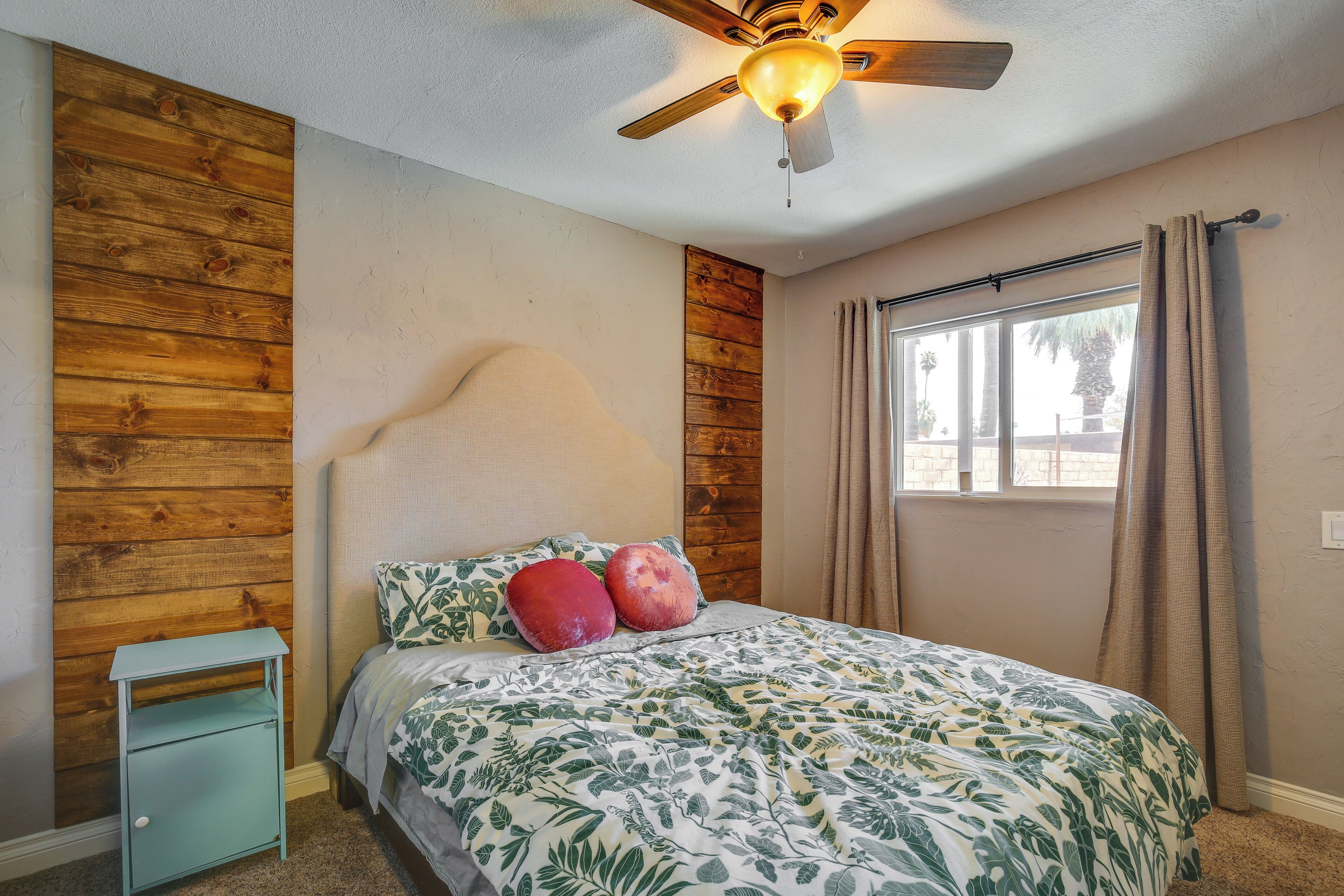 Une chambre avec un mur d’accent en bois, un lit recouvert d’une courtepointe à motifs floraux, une table de chevet et un ventilateur de plafond.