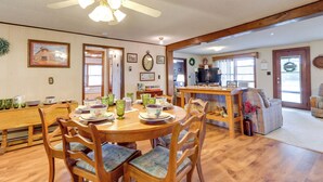 Un coin repas avec une table et des chaises en bois, un ventilateur de plafond et une cuisine en arrière-plan.