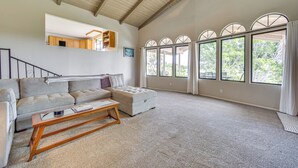 A spacious living room with a high ceiling, a large window with multiple panes, a sofa, a coffee table, and a staircase leading to an upper level. - Secluded Waimea Hideaway w/ Lanai & Views! (Waimea)