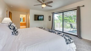 A bedroom with a large bed, a ceiling fan, a TV mounted on the wall, and a sliding glass door leading to a balcony with outdoor furniture. - Secluded Waimea Hideaway w/ Lanai & Views! (Waimea)