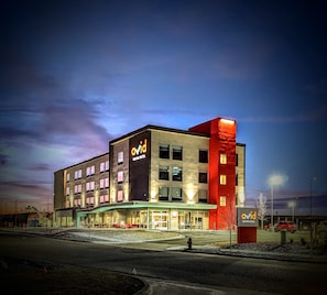 A modern hotel with a prominent red accent on the corner, multiple windows, and a well-lit entrance area.