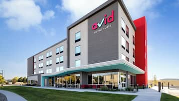 A modern hotel with a prominent red accent on the corner, a covered outdoor seating area, and a clear sky.