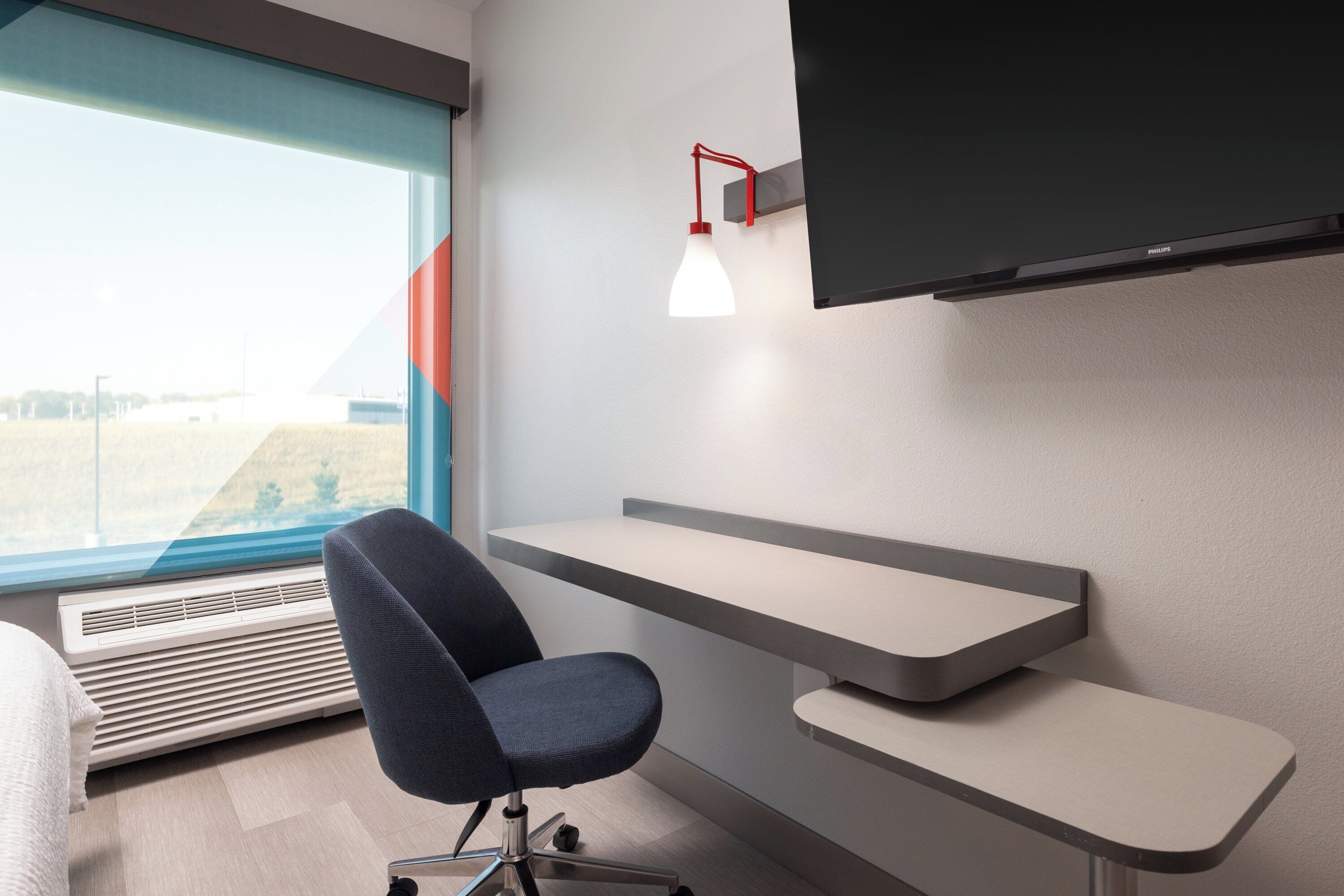 Ein modernes Hotelzimmer mit Schreibtisch, Stuhl und großem Fenster mit Blick ins Freie.