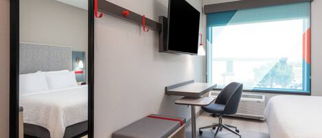 Habitación de hotel con cama, escritorio con silla, televisor montado en la pared y un ventanal con vistas.