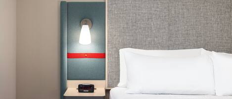 Una habitación de hotel con una cama, una mesita de noche con lámpara y un panel fijado a la pared.