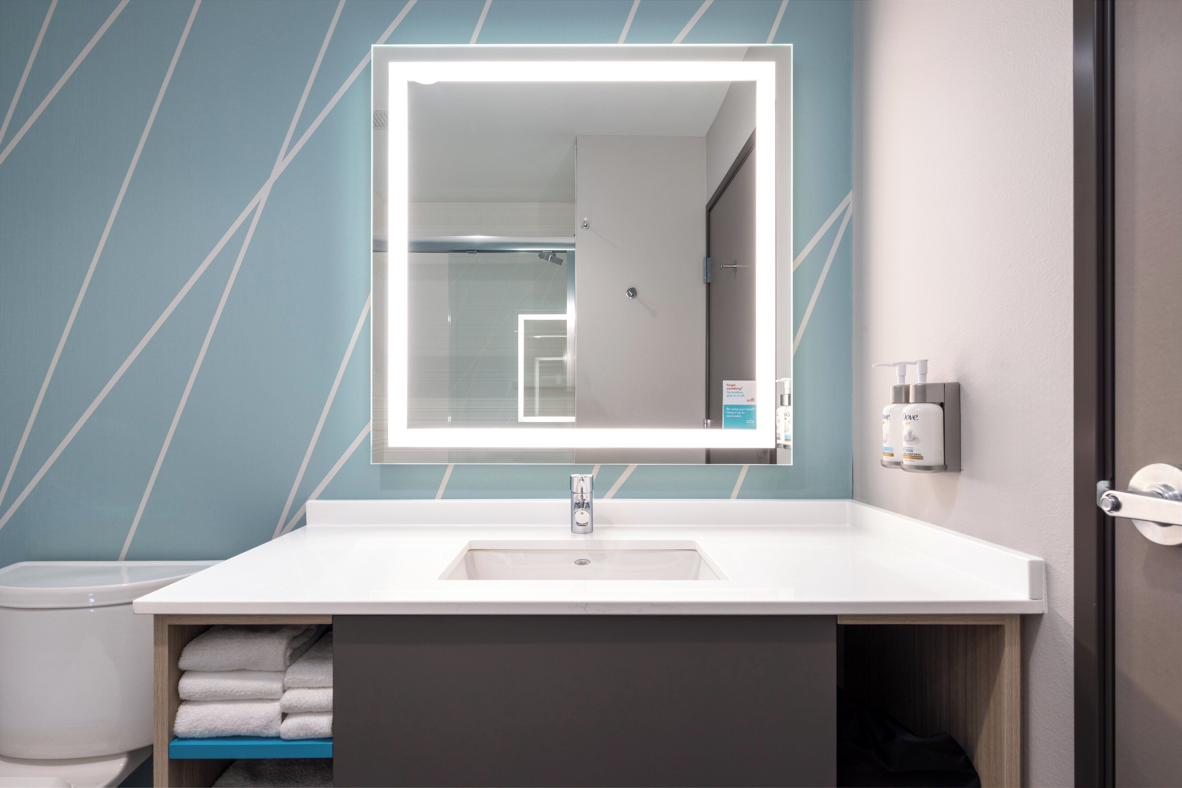 A modern bathroom with a white sink, a large mirror, and a towel rack.
