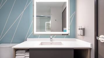 A modern bathroom with a white sink, a large mirror, and a towel rack.