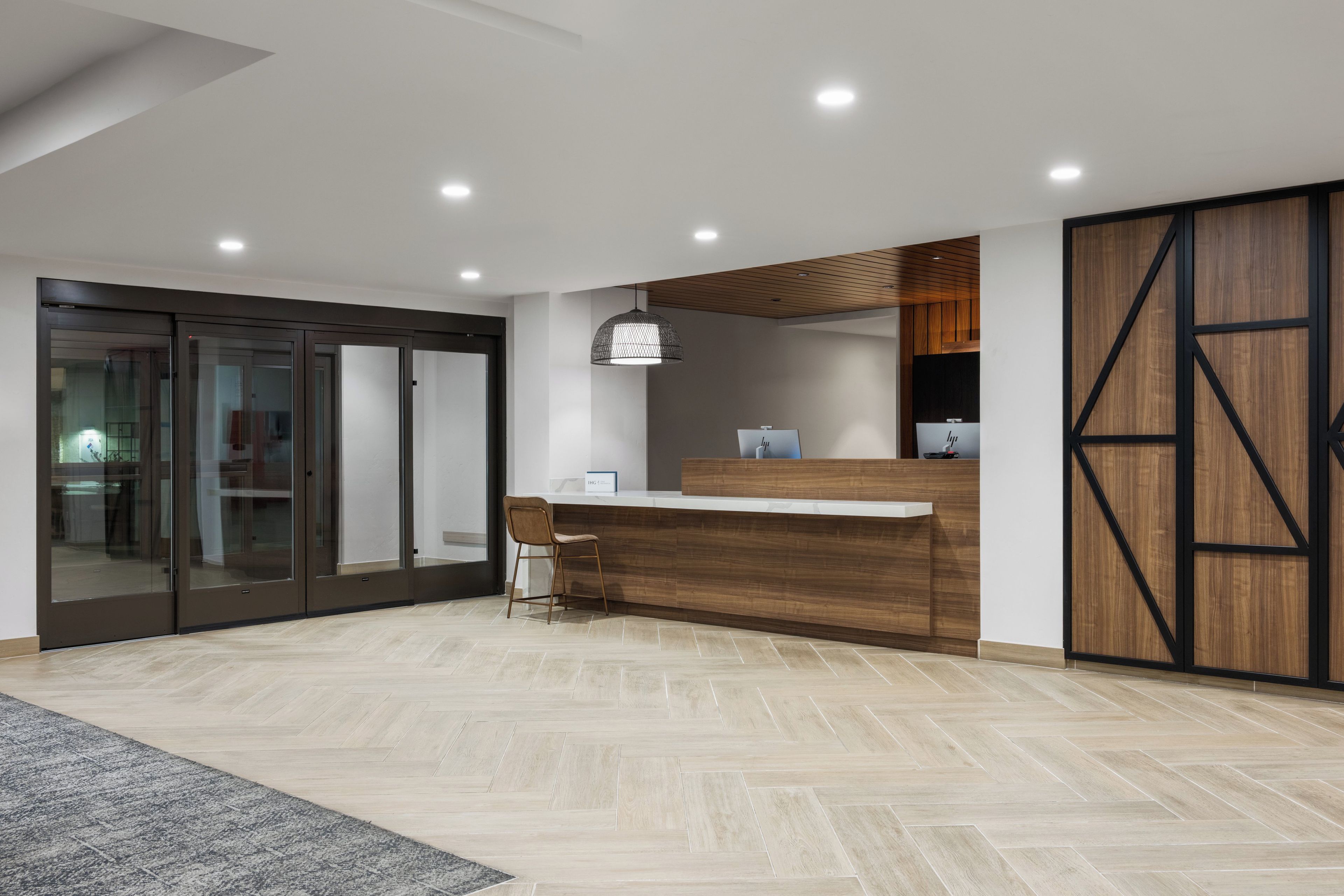 A modern reception area with a wooden reception desk, a single chair, and a large sliding glass door leading to another room.