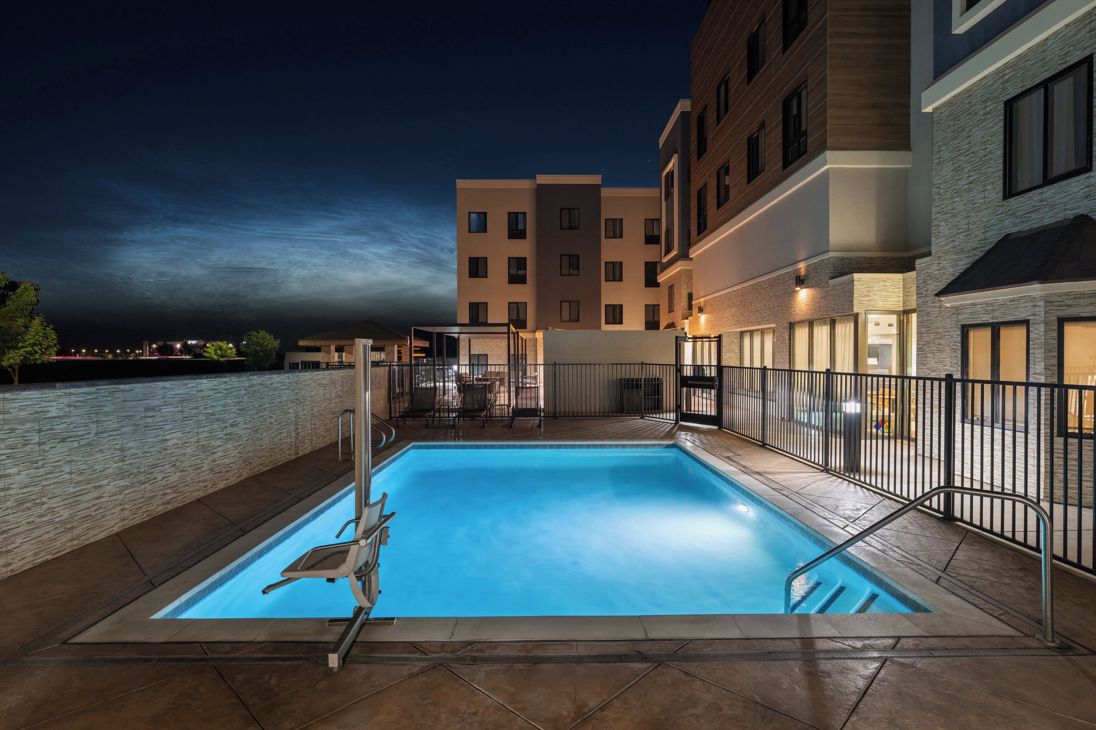 A swimming pool with a chair and a fence, surrounded by buildings.
