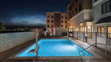 A swimming pool with a chair and a fence, surrounded by buildings.