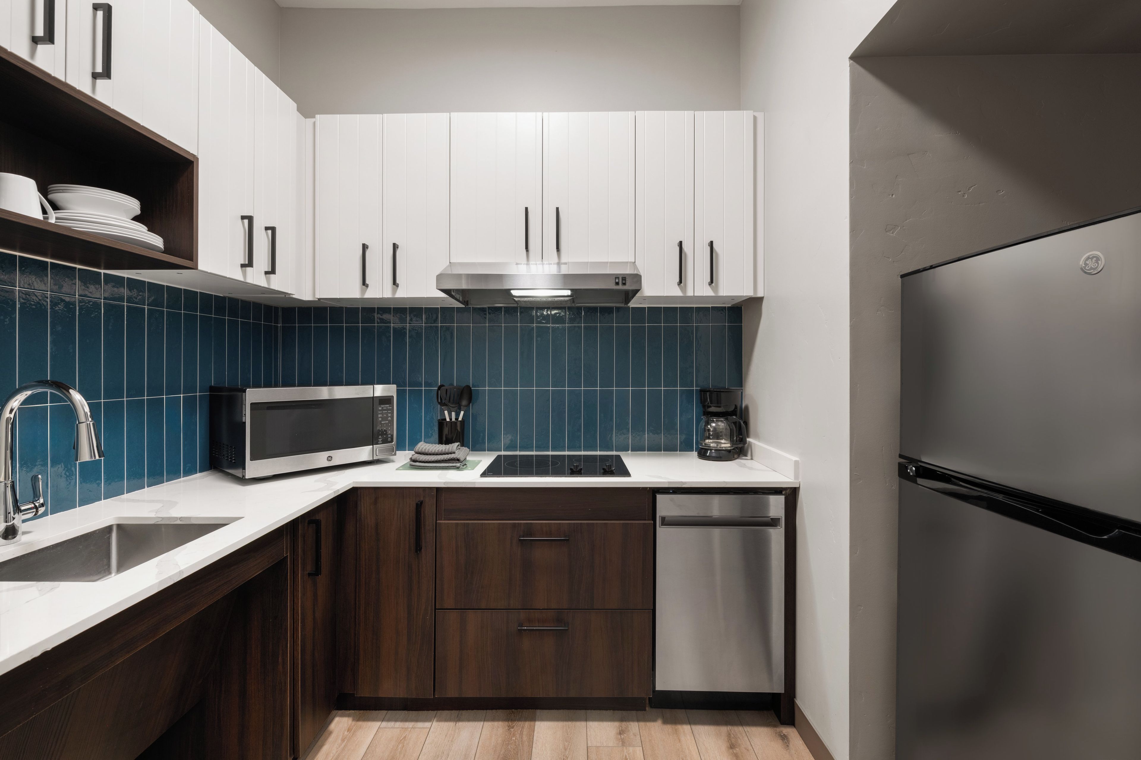 A compact kitchen with white cabinets, a stainless steel refrigerator, a microwave, and a coffee maker.