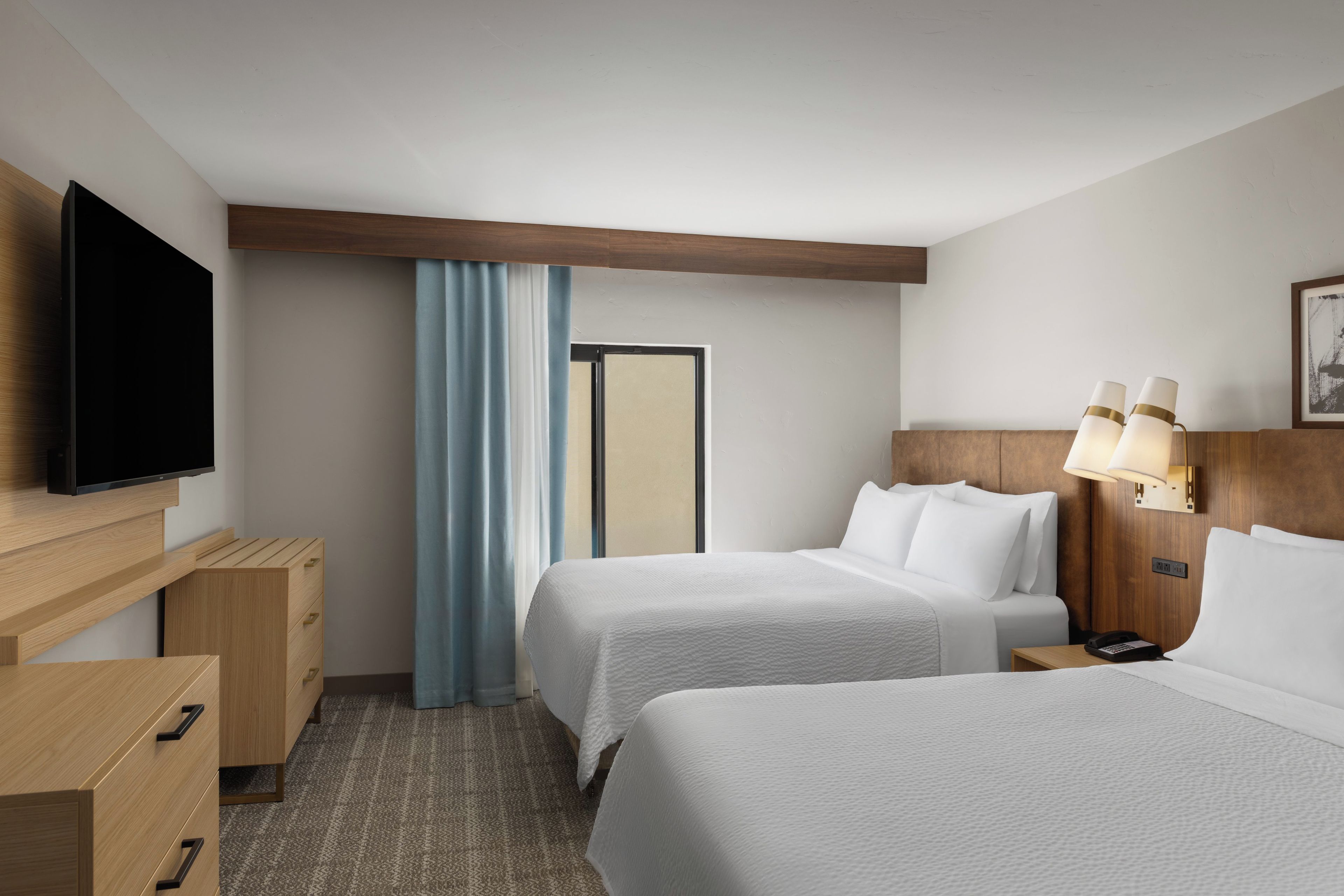 Una habitación de hotel con dos camas, televisión, escritorio con cajones, lámpara y puerta.