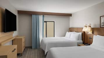 Una habitación de hotel con dos camas, televisión, escritorio con cajones, lámpara y puerta.