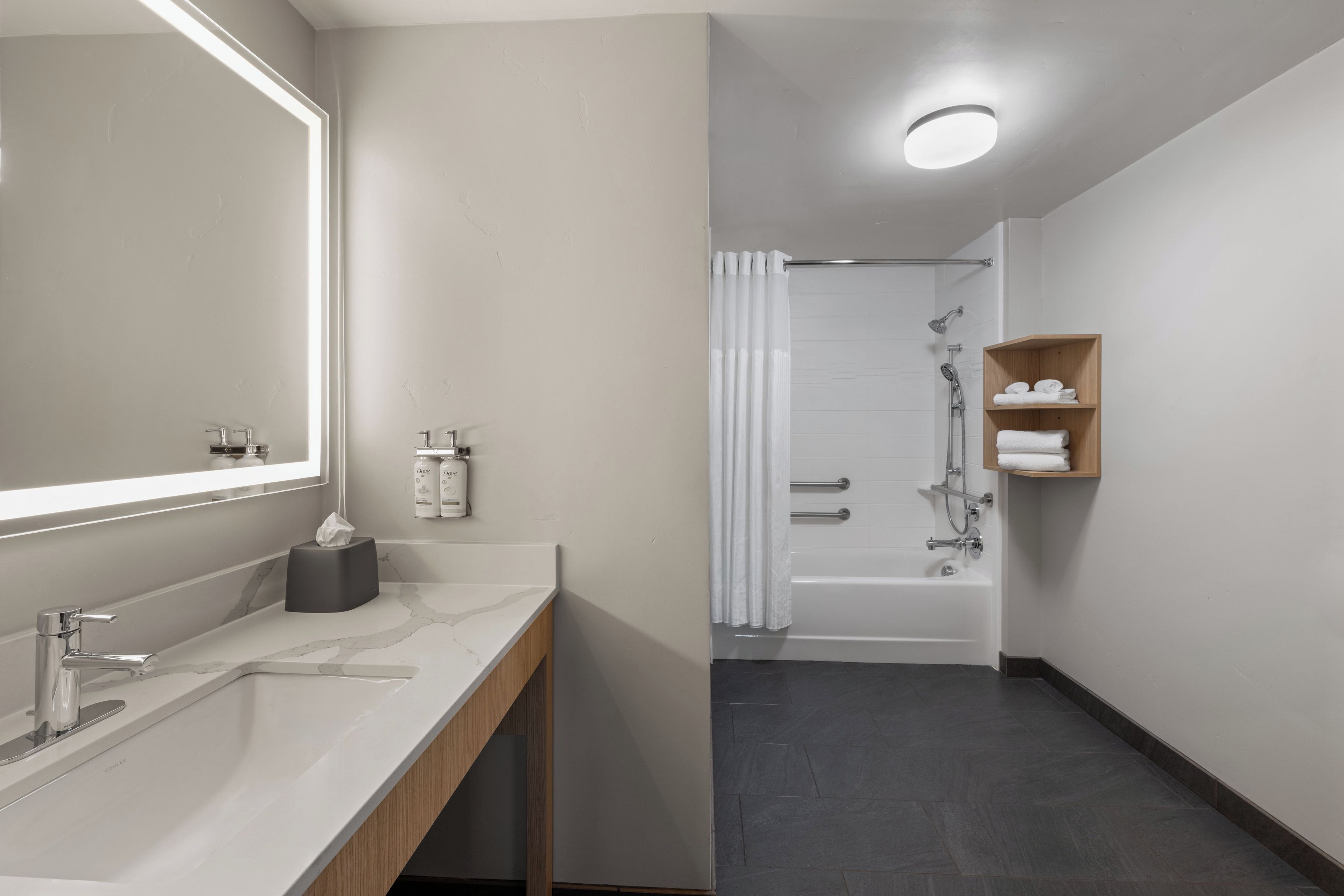 A modern bathroom with a large mirror, dual sinks, a vanity, a shower area, and a wooden shelf with towels.