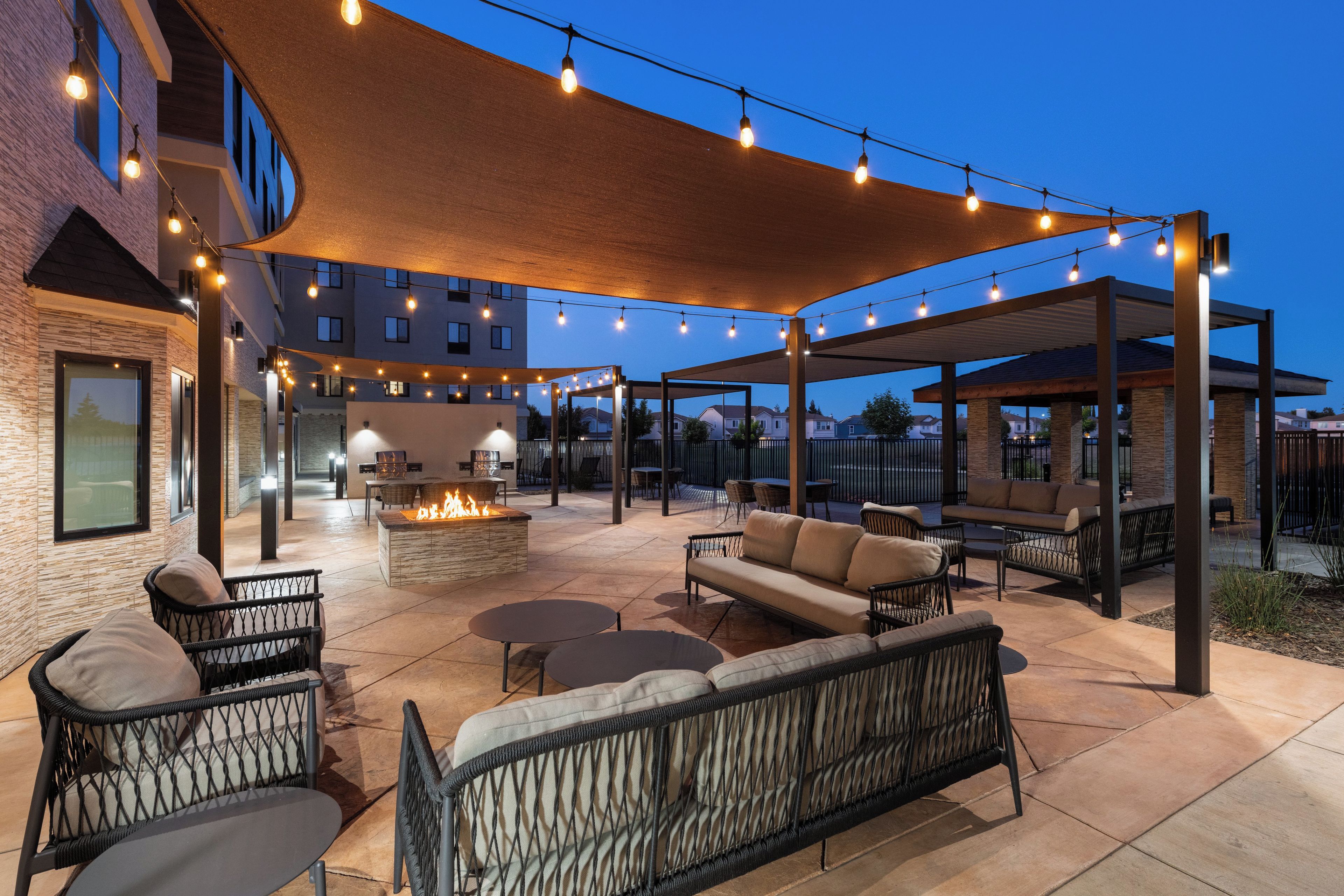 An outdoor patio area with seating, a fire feature, and string lights.