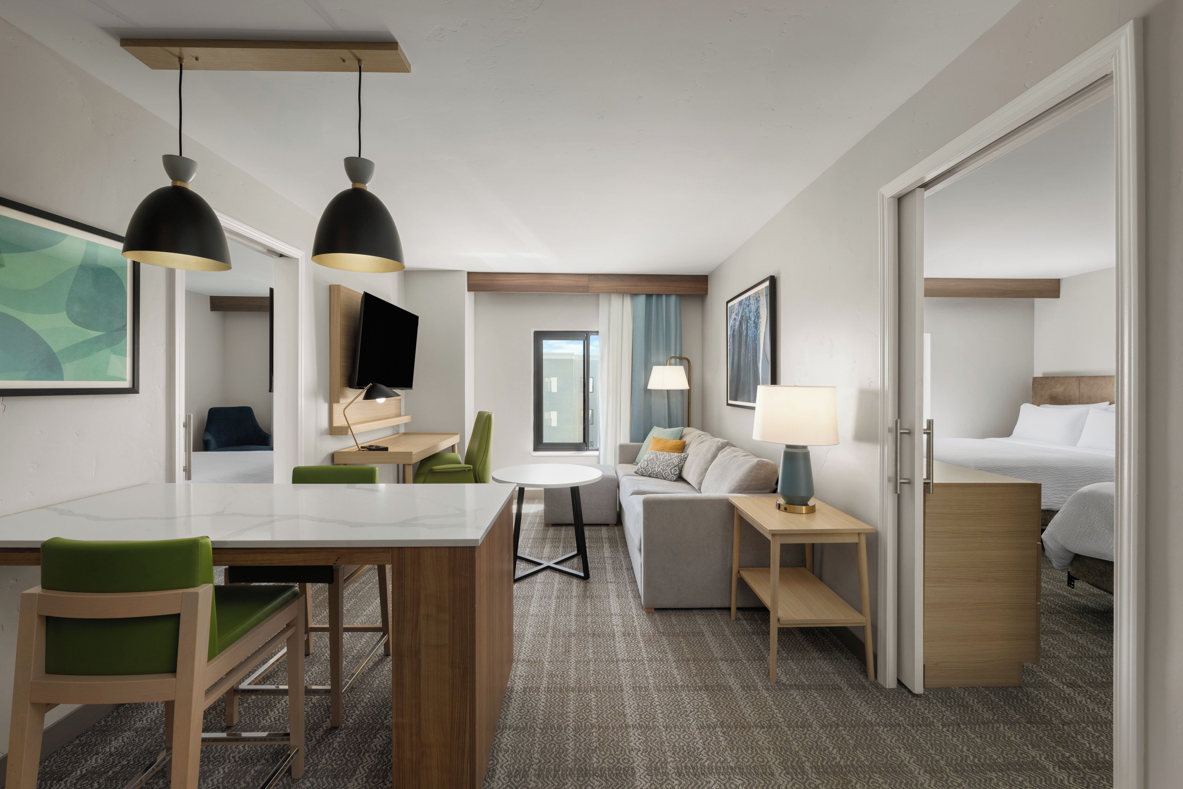A hotel room with a dining area, a sofa, a bed, and a TV.
