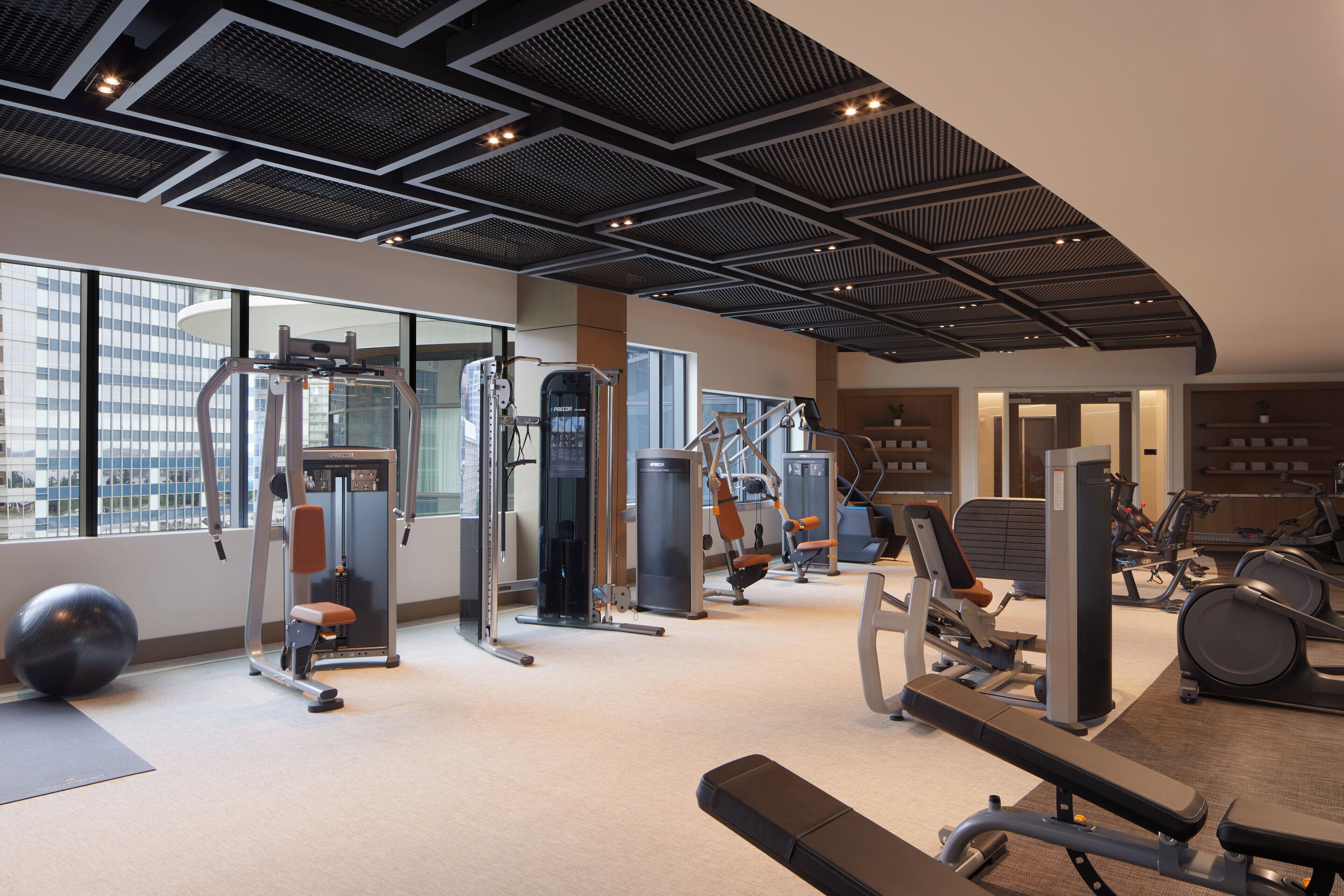 Ein modernes Fitnessstudio mit verschiedenen Trainingsgeräten, großen Fenstern und hoher Decke.