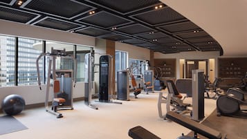 Ein modernes Fitnessstudio mit verschiedenen Trainingsgeräten, großen Fenstern und hoher Decke.