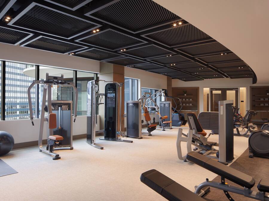 Ein modernes Fitnessstudio mit verschiedenen Trainingsgeräten, großen Fenstern und hoher Decke.