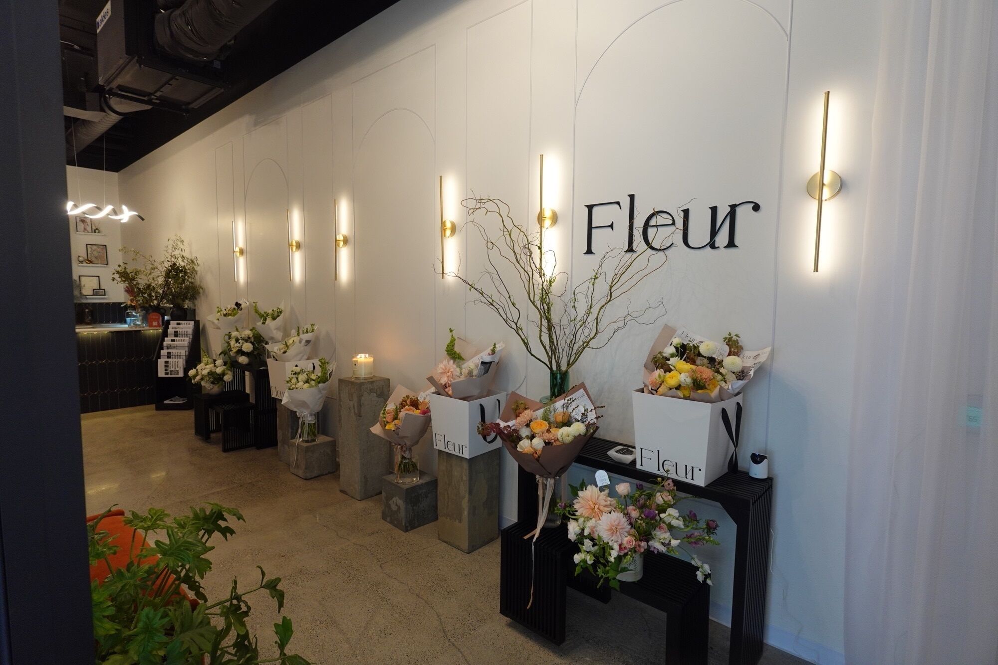 A floral display with the word "Fleur" on the wall, surrounded by various flower arrangements on pedestals.