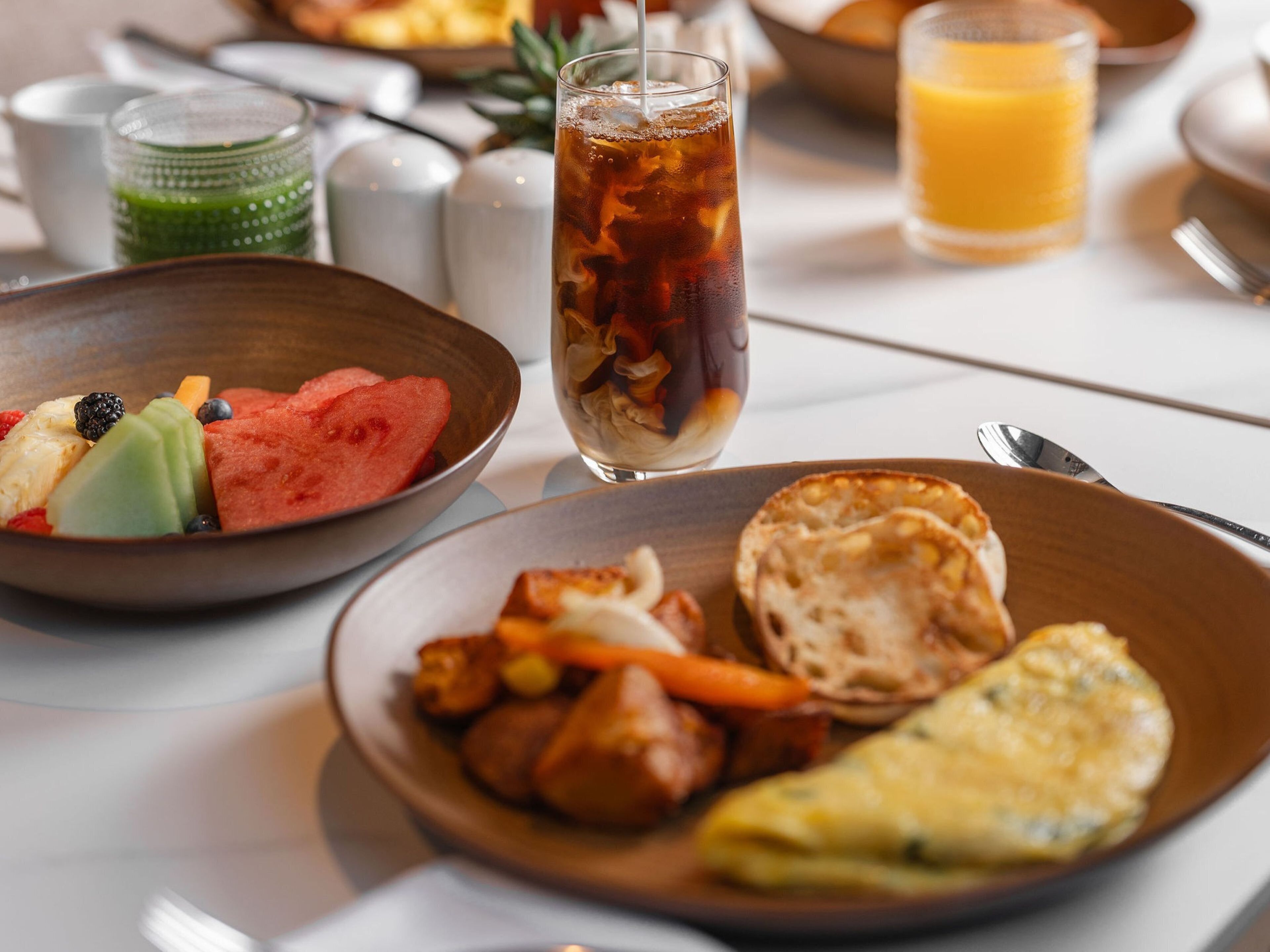 A breakfast setting with various dishes, including a bowl of fruit, a glass of iced tea, and a plate with toast and eggs.