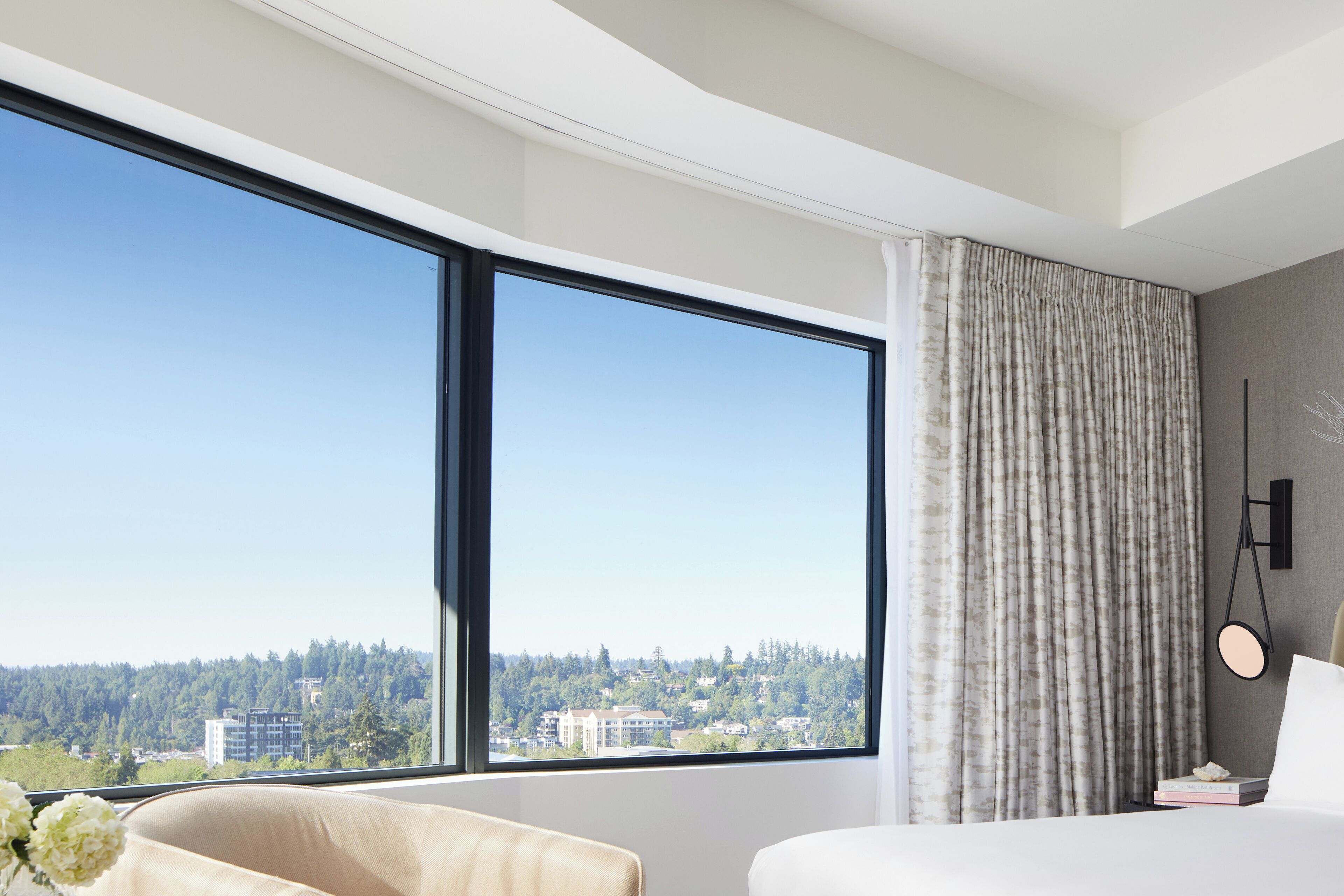 Habitación de hotel moderna con un ventanal grande que ofrece vistas a la ciudad, una cama, una mesita de noche y una silla.