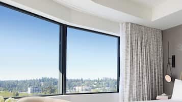 Habitación de hotel moderna con un ventanal grande que ofrece vistas a la ciudad, una cama, una mesita de noche y una silla.