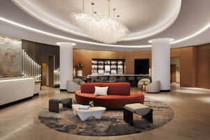 A modern lobby with a red sofa, a white reception desk, and a bar area in the background.